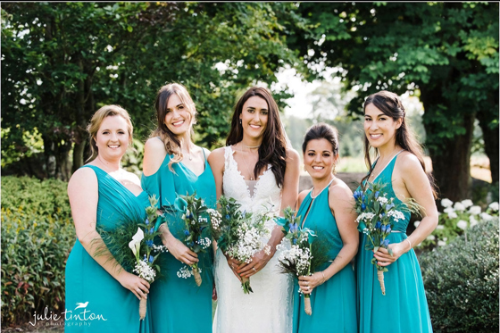 Bridal party pose together in gardens of wedding venue. The bridesmaids are wearing teal dresses and everyone's makeup is by Jennifer Louise Studio.